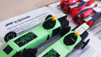 Four mini cars with toy people on top of F1 related paperwork.